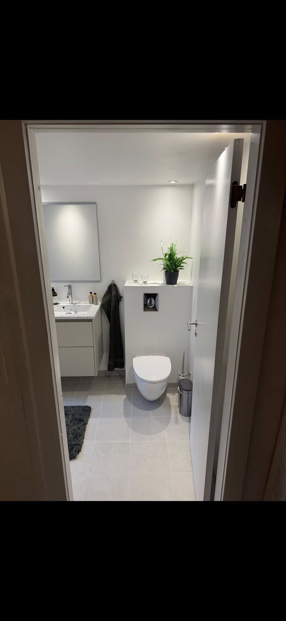 Samme badeværelse efter renovering – vægthængt toilet, ny vask og lyse fliser