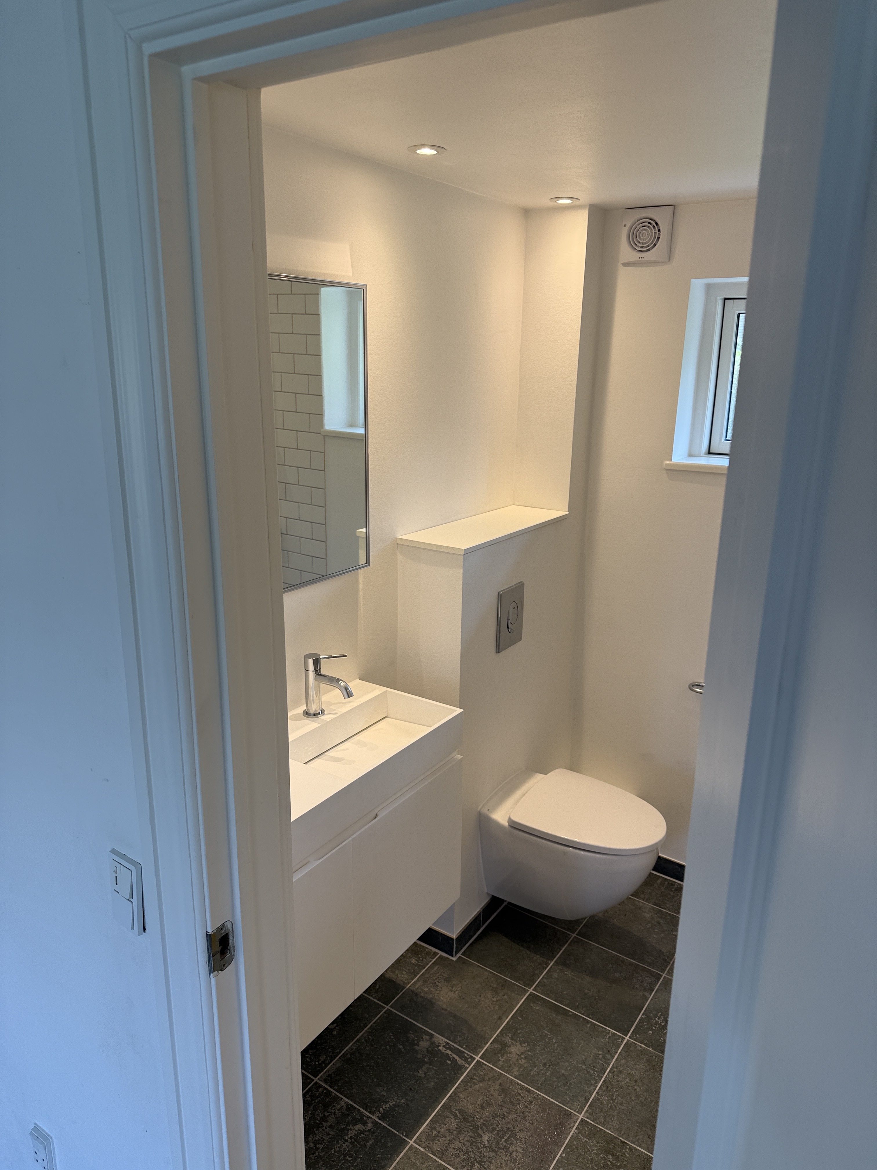 Smalt badeværelse med vægthængt toilet, håndvask og lyse vægge